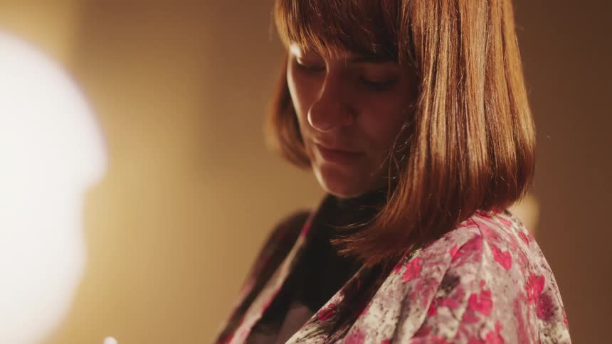 Woman in a pink patterned blouse looks down as she writes with a white pen