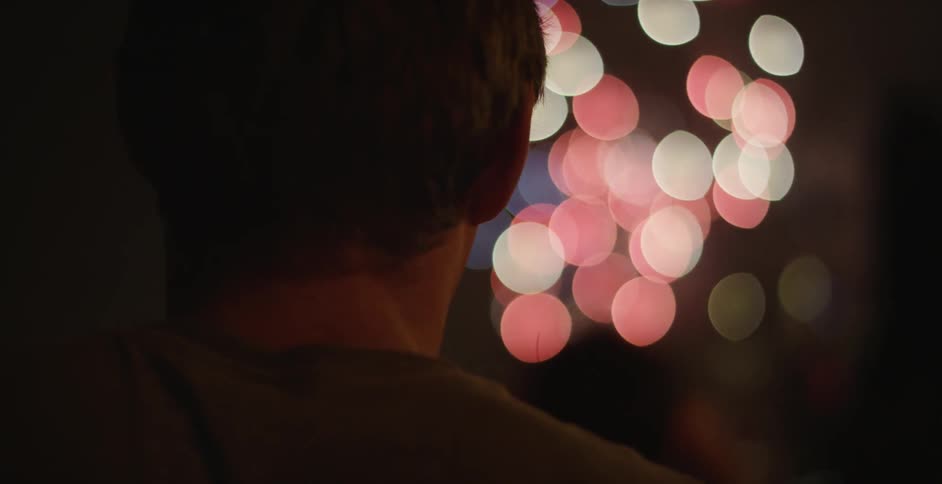 Fireworks are exploding in a night sky as a man watches on