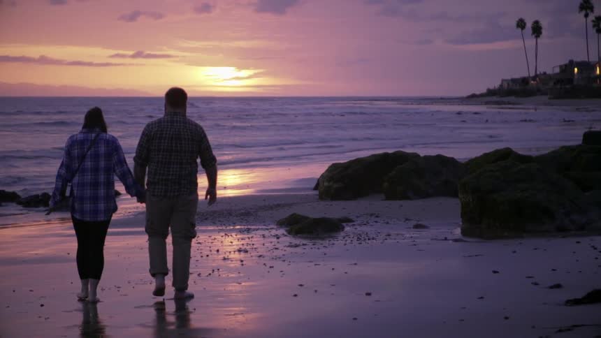 A couple walk on the beach barefoot