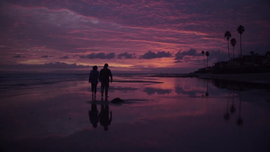 A couple walks on the beach at sunset