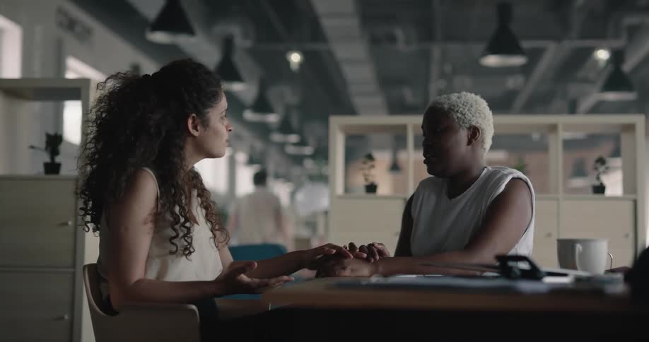 Sad woman consoles a friend or coworker while sitting at a desk in the office