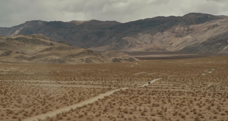 Aerial view of a jeep traveling on a dirt road in the desert and a mountain ridge in the distance