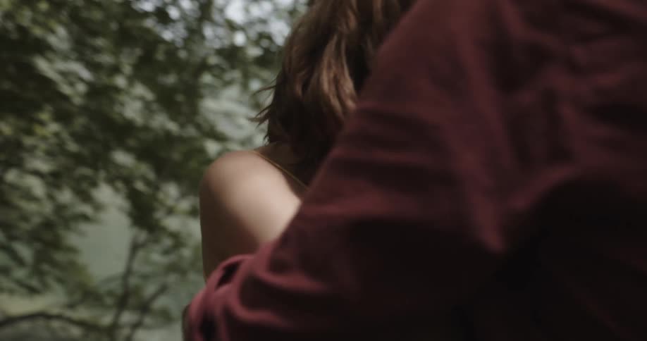 A woman tries to push her boyfriend away while he comforts her in the woods near a lake