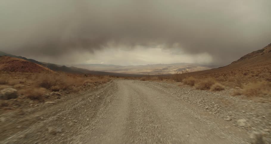 Traveling on a dirt road in the desert with mountains in the distance as dark clouds move overhead