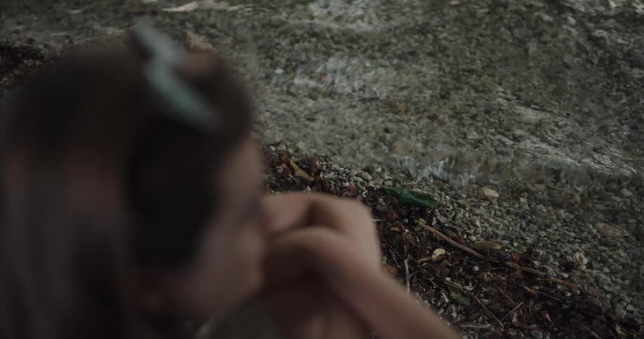 A woman sits on the ground on the shore of lake while lost in thought