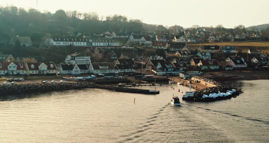 A boat sails back toward a harbor near a dense neighborhood