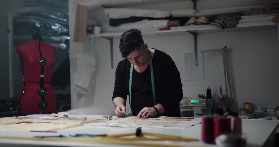 Tailor with black sweatshirt and green meter works and makes measurement in tailor shop