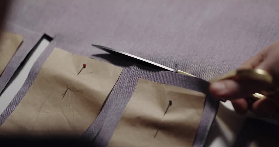 Person cuts fabric pieces based on pinned paper pattern plus seam allowance