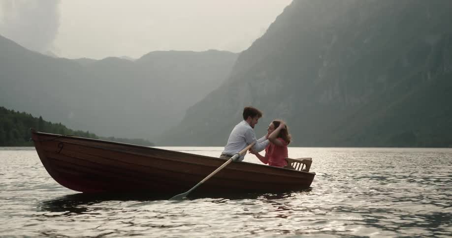 Young couple in love kiss and hug inside a rowboat on a lake in the mountains at morning