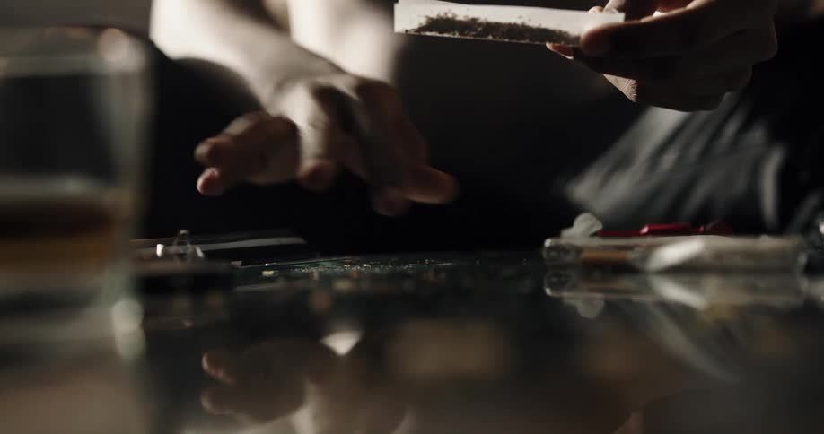 A man rolls a marijuana cigarette while sitting on the couch