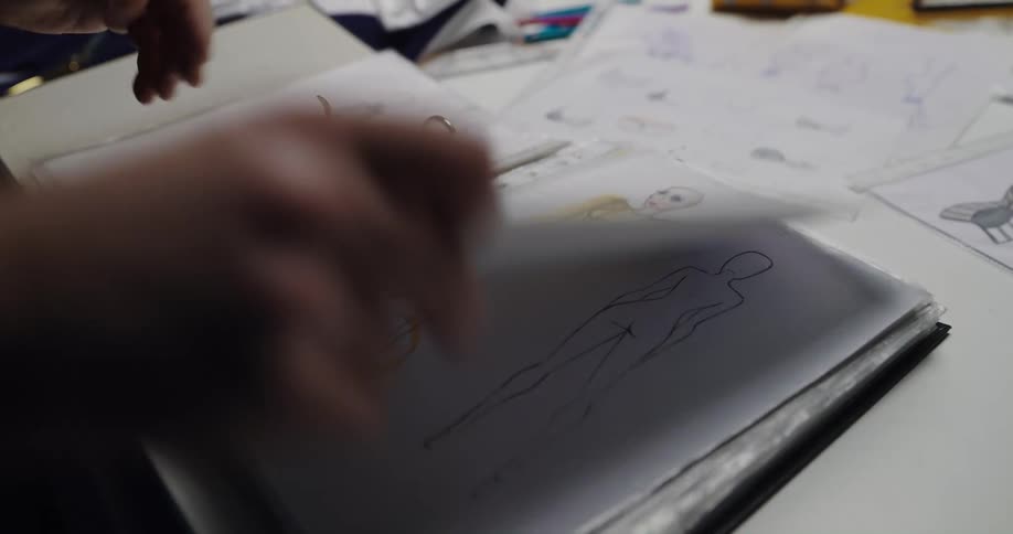 A man flips through a binder of fashion sketches and selects several