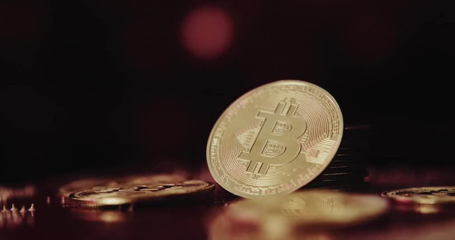 A stack of golden coins with the printed bitcoin logo on them in front of a screen displaying a line graph