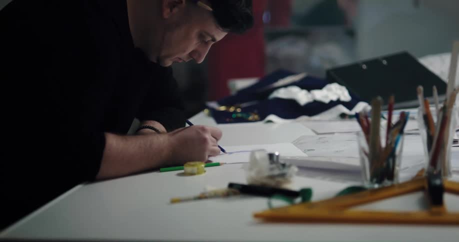 Tailor with black sweatshirt draws in notebook at tailor shop