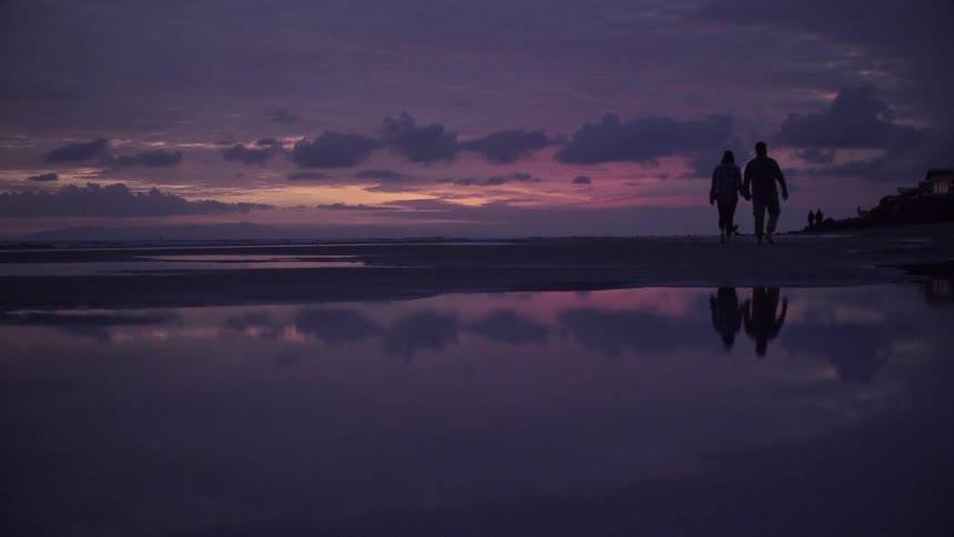 Two people walk on the beach at dawn