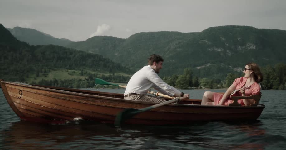 Man rows a rowboat while a woman sits across from him and plays a ukulele