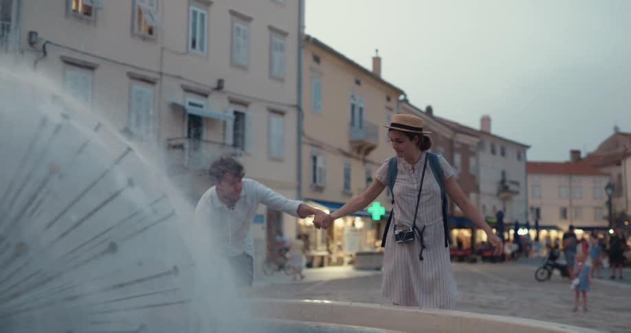 A woman embracing a man before climbing atop a water fountain in a city during the day