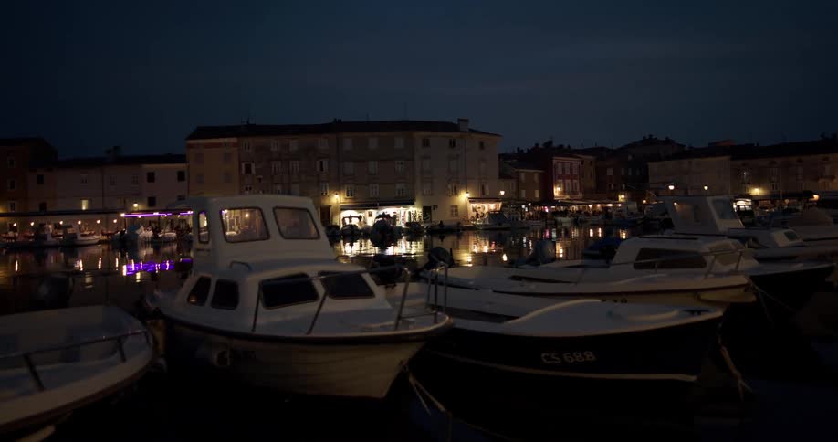A line of boats moored in a marina in a city at night