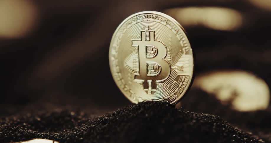 Gold bitcoin standing on a mound of black particles