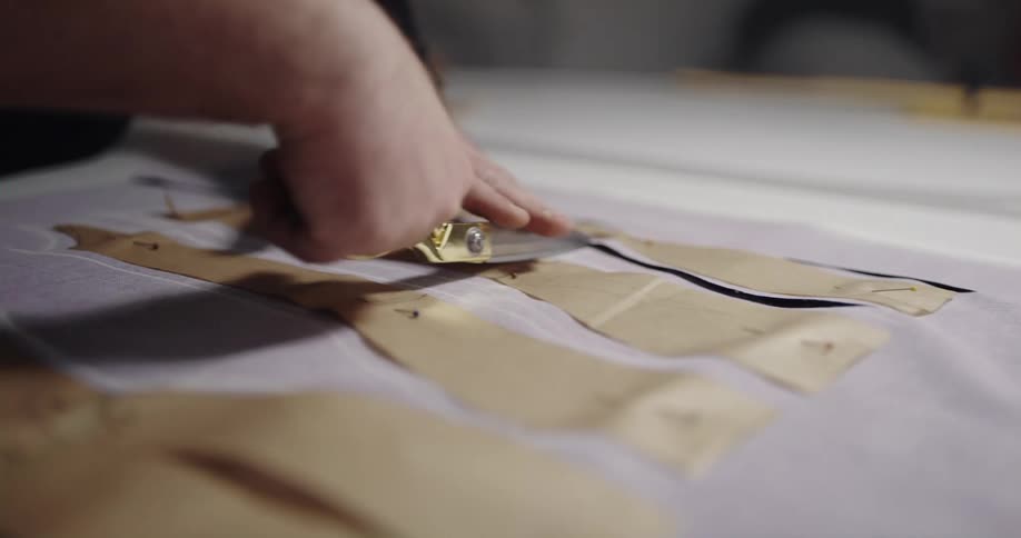 Tailor wearing black sweatshirt cuts a piece of cloth with scissors in tailor shop