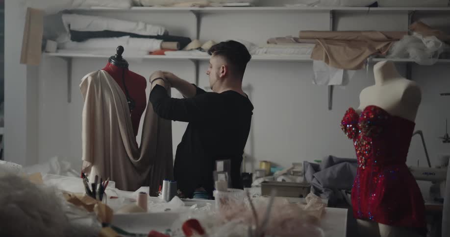 A fashion designer pins a fabric to the shoulders of a mannequin