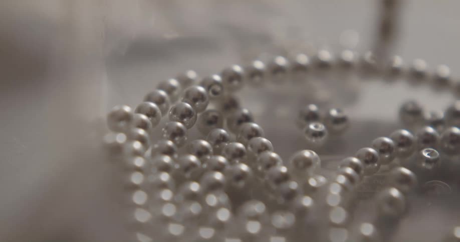 A person removes small silver beads from a necklace and drops them onto a table