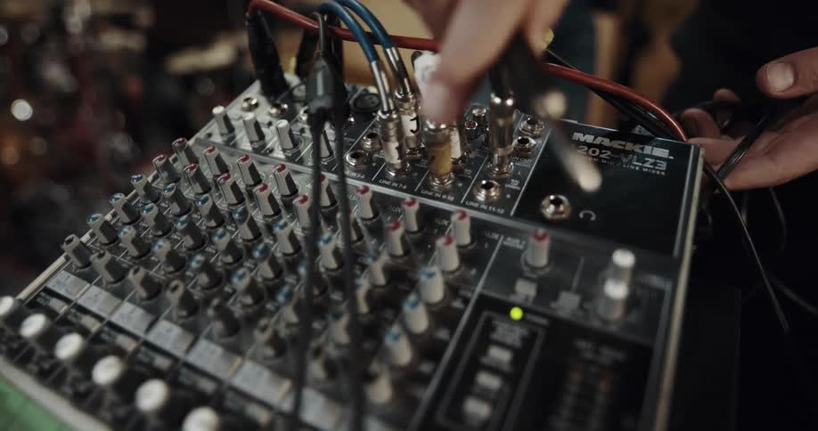 A person inserts a pair of plugs into two of the sockets on a compact sound mixing board