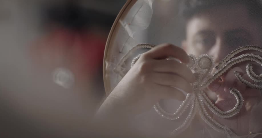 A fashion designer uses an embroidery hoop as he sews on beads and pearls in the shape of a butterfly