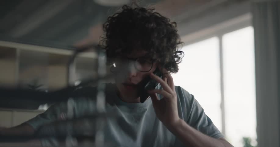 A man is sitting indoors and talking on the phone