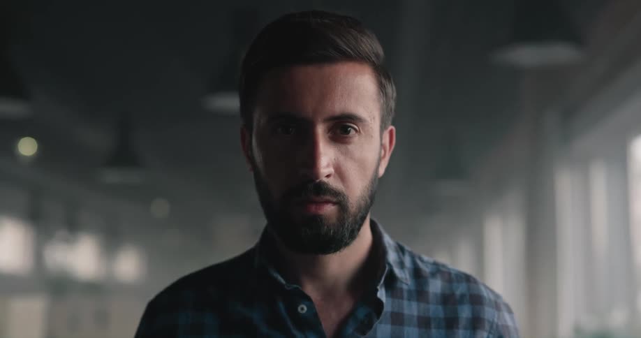 A man with a beard slowly looks upwards while posing for the camera