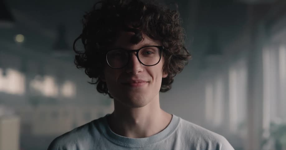 A teenage boy wearing glasses looks up and smiles