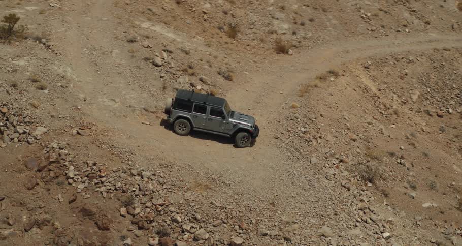 A rugged jeep sits idle on a dirt road that twists its way down a rocky mountainous area