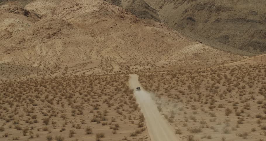 A jeep is traveling on a dirt road through the desert and there are mountains in the distance