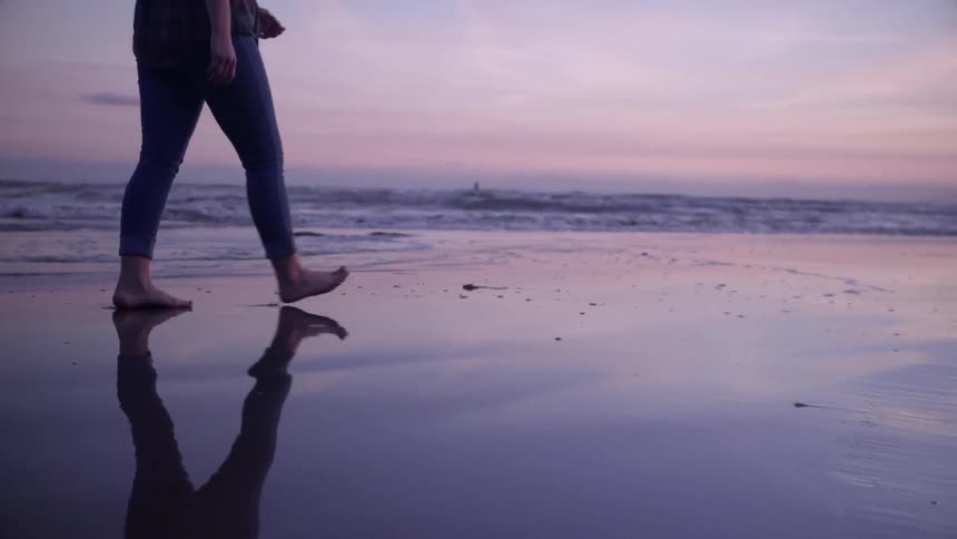 A person is walking along the sand of the shore