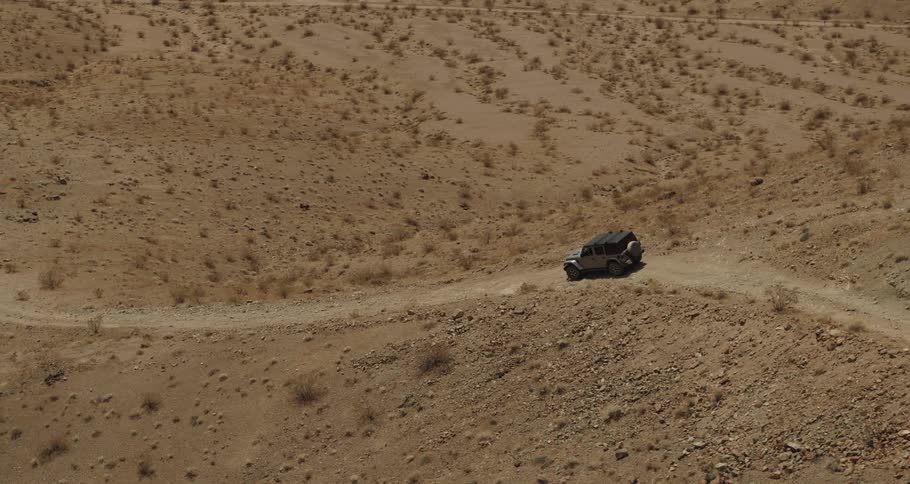 Vehicle travels on a dirt road on a hill in the desert