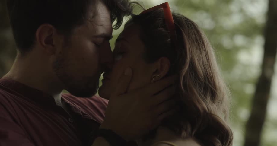 Man with beard and red t shirt kisses and makes up with woman wearing red glasses in the woods