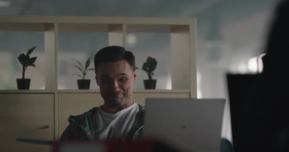 Man working at the office sitting at a desk in front of a laptop talks to a coworker