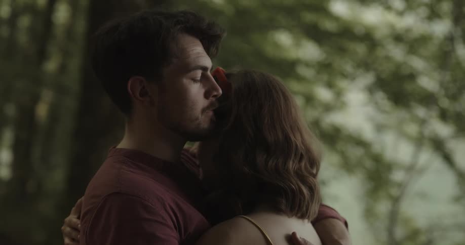 Close up of a man consoling his partner with a hug and kisses on her forehead in the forest