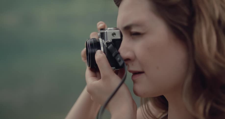 A woman is outside and she puts a camera to her face and takes a picture