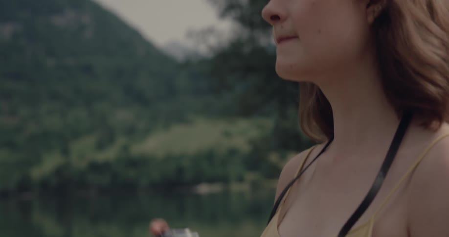 Woman standing near the water of a lake using her digital camera to take pictures of the surroundings