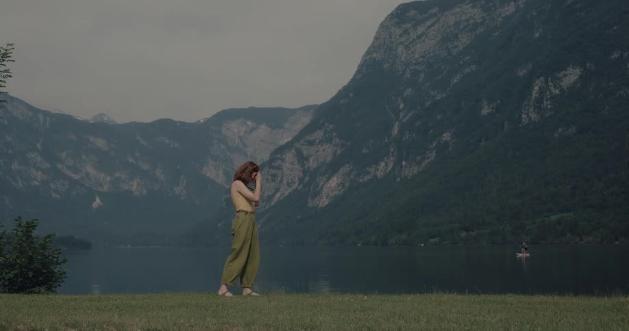 A young woman standing before a mountain range uses her camera to take some photographs