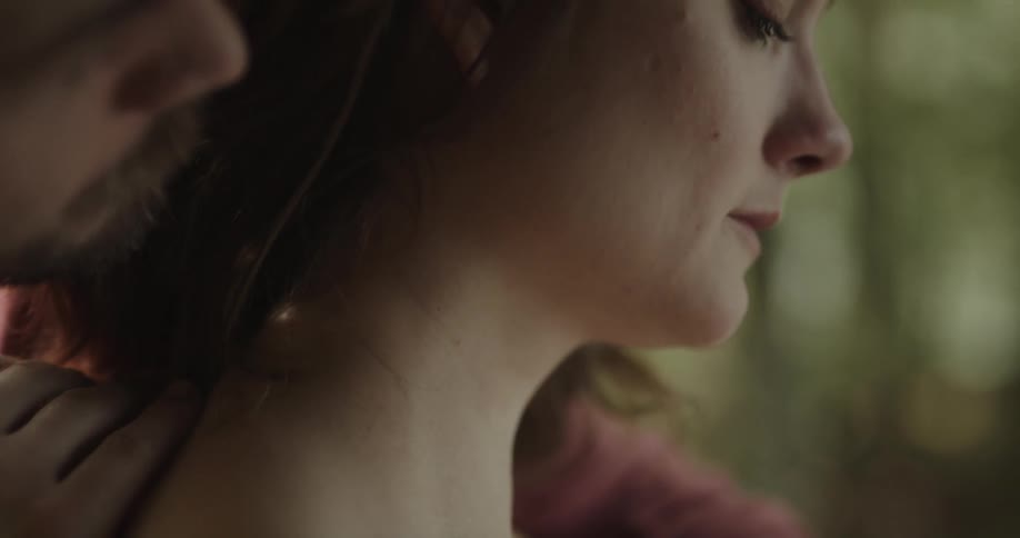 Man strokes the hair and kisses the neck of woman standing sadly among trees