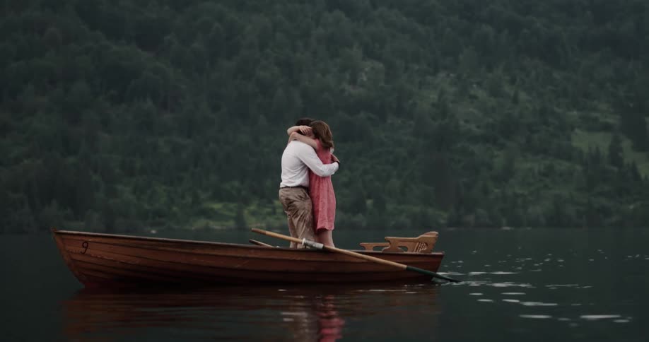 Man and woman standing in a wooden canoe in the middle of a lake kissing and hugging each other