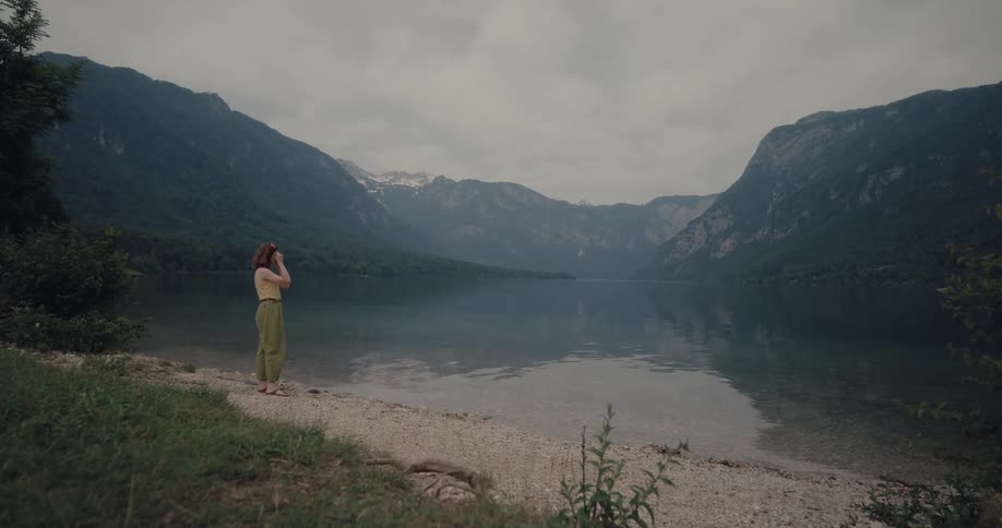 White woman standing near the water of a lake taking pictures of the surroundings with her digital camera