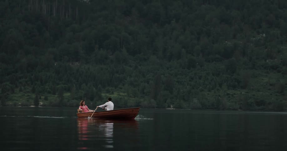 Couple sitting on a wooden canoe with the man rowing in the middle of a lake
