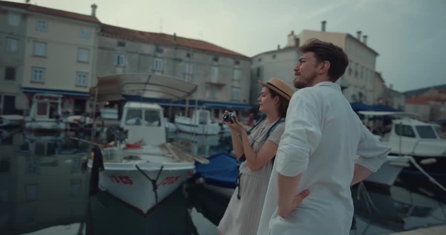 A woman takes a photograph of a marina before being kissed by a man standing beside her