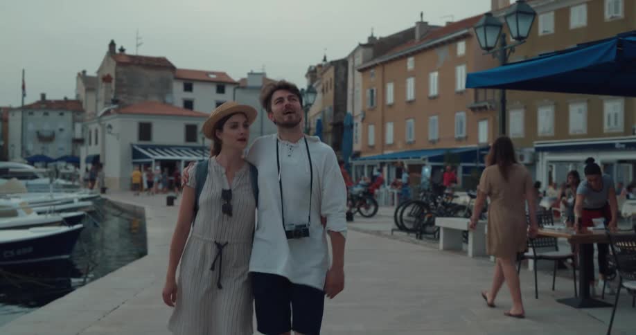 Young happy couple on vacation kiss while hugging and walking near a pier in a small town