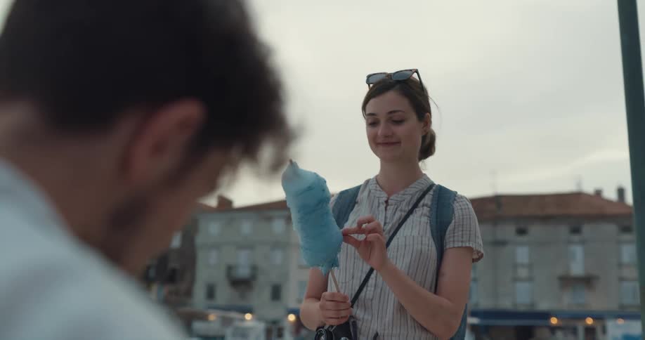 Man playing ukulele while woman eating cotton candy watches then tips him