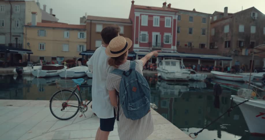 A man and woman hold hands while walking down a pier lined with boats