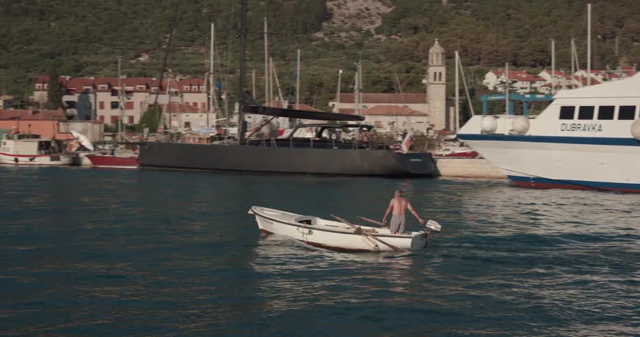 Man stands while motoring across water in boat near seaside town