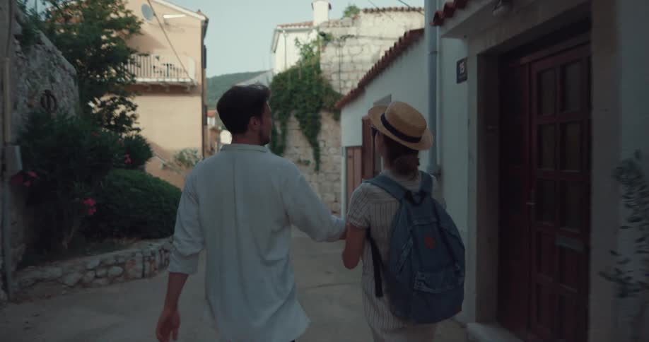 A couple walk through a quaint village full of stone houses and greenery